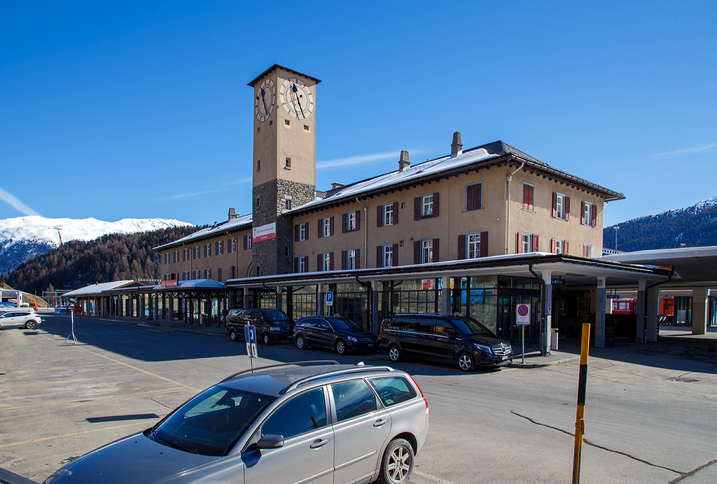 Der RhB Bahnhof St. Moritz blick von der Vorplatzseite mit dem Empfangsgebäude und links dem Güterschuppen am 20 Februar 2017. 

Der Bahnhof St. Moritz ist der Bahnhof des Kurortes St. Moritz im Oberengadin im Kanton Graubünden. St. Moritz ist nach dem heiligen Mauritius benannt, der auch im Wappen abgebildet ist. Er ist aber auch hier an den Uhrenturm abgebildet. Der Bahnhof wird von der Rhätischen Bahn (RhB) betrieben und liegt auf 1.775 m über Meer am nordwestlichen Hang des Tales unmittelbar oberhalb des St. Moritzersees beim Ausfluss des Inn. Er ist Endbahnhof der Albulabahn und der Berninabahn. Da diese mit unterschiedlichen Stromsystemen betrieben werden, ist er zugleich ein Systemwechselbahnhof.

Hinten links sieht man auch die Standseilbahn Muottas-Muragl-Bahn (MMB). Die Standseilbahn führt von Punt Muragl (1.739 m ü. M.) zwischen Samedan und Pontresina, auf den Muottas Muragl (2.448 m ü. M.). Die Bahn hat eine Streckenlänge von 2.199 m und überwindet eine Höhendifferenz  von 709 m. Sie ist die älteste Bergbahn im Engadin und feierte 2007 ihr 100-jähriges Bestehen.

Der Bahnhof St. Moritz:
Der Bahnhof wurde als Durchgangsbahnhof gebaut, da anfänglich eine Verlängerung der Strecke Richtung Maloja geplant war. So führte ein Gleis von der Westseite des Bahnhofs zunächst über eine Brücke und anschließend fast in den Hang hinein. An dieser Stelle war das Portal eines Tunnels geplant, der das Ortszentrum von St. Moritz unterfahren sollte.

Im Hinblick auf die Skiweltmeisterschaften 2017 in St. Moritz wurde der Bahnhof zwischen 2014 und 2017 zu einem Kopfbahnhof mit schienenfreien Zugängen und einem Querperron ausgebaut. Die drei neuen, überdachten Perrons (Bahnsteige) an fünf Personengleisen sind behindertengerecht gestaltet. Wobei die alte Gestaltung mir persönlich besser gefiel. Das Bahnhofgebäude blieb unverändert, während der Bahnhofplatz mit einem Busterminal neu konzipiert wurde. Der Güterschuppen wird für bahneigene Nutzung verwendet. Für die diversen neuen Abstellgleise musste die RhB eine 250m lange Stützmauer entlang der Kantonsstraße erstellen lassen.

Baulich:
Das stattliche Aufnahmegebäude liegt auf der Bergseite der Gleisanlagen und besitzt einen Hausbahnsteig. Dazu existieren ein Mittelbahnsteig für die Züge des RhB-Stammnetzes und ein weiterer für die Züge der Berninabahn. Östlich des Empfangsgebäudes steht der Güterschuppen mit Rampe (hier links im Bild), eine weitere offene Verladerampe liegt im östlichen Bahnhofsteil zwischen den beiden Streckenausfahrten. Daneben sind umfangreiche Abstellanlagen vorhanden.

Die Berninabahn führt unmittelbar nach dem Bahnhof über die Innbrücke und kurz darauf in den 689 m langen Charnadüra-Tunnel II. Unter der Bahnbrücke führt eine Straßenbrücke in einem anderen, sich kreuzenden Winkel über den Inn. Die Albulabahn führt gleich nach dem Bahnhof in den 114 m langen Argenteri-Tunnel und kurz darauf durch den 448 m langen Charnadüra-Tunnel I.

Das Empfangsgebäude wurde 1927 gebaut und ersetzte das erste Empfangsgebäude.

Betrieblich:
Der Bahnhof ist betrieblich zweigeteilt, da die beiden Strecken mit unterschiedlichen Stromsystemen betrieben werden. So ist die zum RhB-Stammnetz (StN) gehörende Albulabahn mit 11 kV 16⅔ Hz Wechselstrom, die Berninabahn (BB) dagegen mit 1 kV Gleichstrom elektrifiziert. Für Rangiermanöver waren aus diesem Grund 2017 noch dieselbetriebene Rangierfahrzeuge (z.B. RhB Tm 2/2) stationiert.

Der Fahrplan besteht aus einem stündlichen InterRegio über die Albulabahn nach Chur und einem stündlichen Regio nach Pontresina, der meistens nach Tirano weiterfährt. Der InterRegio hat in Samedan Anschluss an die Züge ins Unterengadin. Zusätzlich verkehren RegioExpress nach Zernez (– Vereinatunnel –) Klosters – Landquart. Der Bahnhof ist der offizielle Start- und Endpunkt des Glacier-Expresses. Aber auch die Triebwagen, die den Bernina-Express führen, starten und enden hier, während die Panoramawagen von und nach Chur beziehungsweise Davos von einem Zweistrom-Triebzug des Typs ABe 8/12 «Allegra» gezogen werden und direkt nach Pontresina fahren.